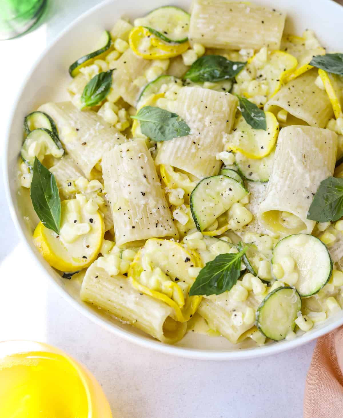 a white bowl filled with zucchini, basil, rigatoni, cream and parmesan cheese