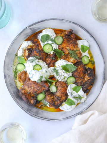 a plate of smokey paprika chicken with dollops of cucumber tzatziki, fresh mint and cucumber slices on a blue background with a white linen napkin