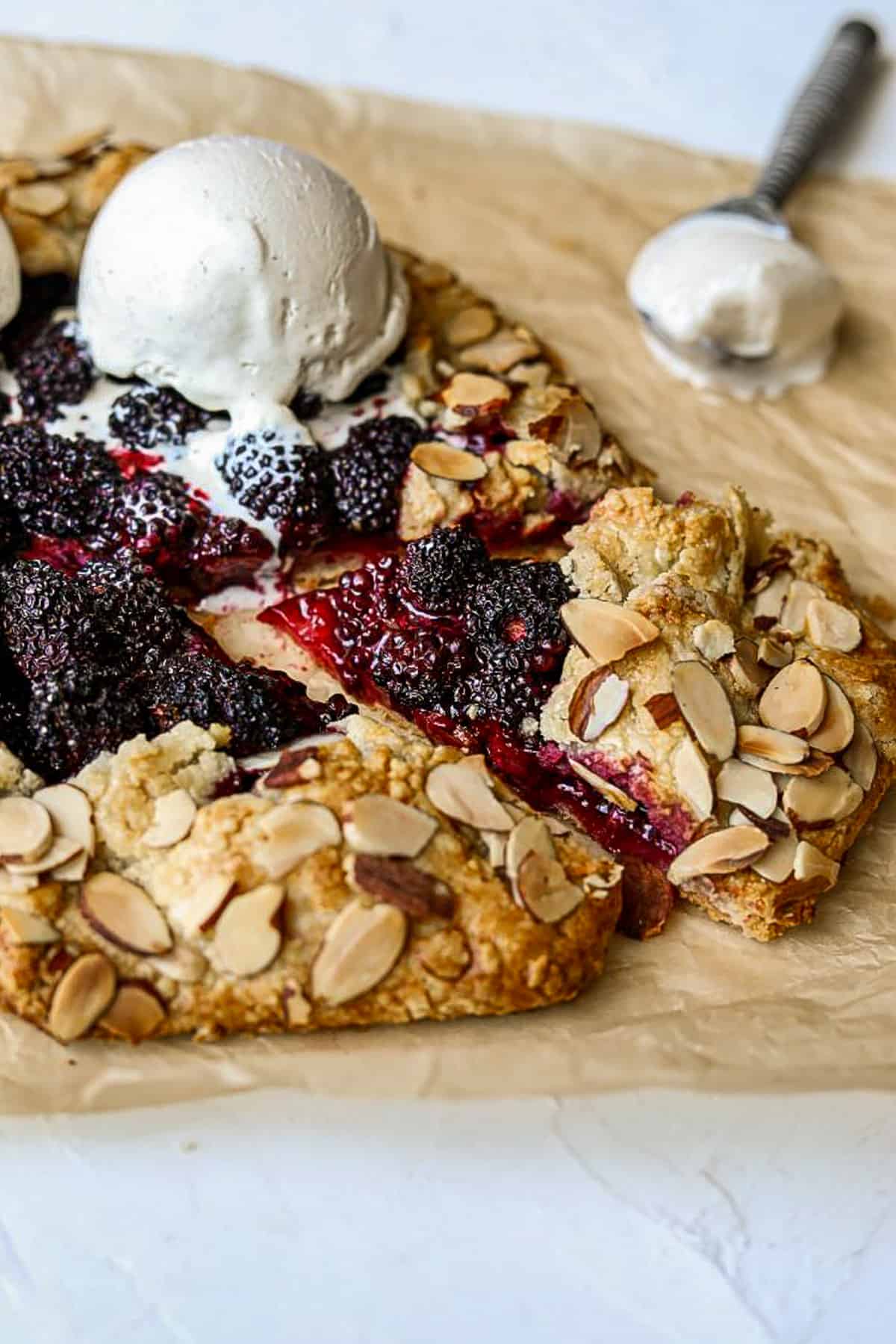a wedge of blackberry crostata with a scoop of vanilla ice cream on brown parchment paper