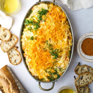 a copper baking dish filled with pimento cheese crab dip surrounded by sliced bread and two beer glasses