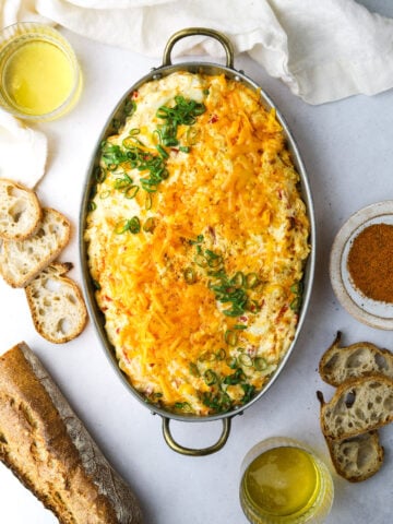 a copper baking dish filled with pimento cheese crab dip surrounded by sliced bread and two beer glasses