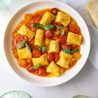 a white bowl of ricotta gnocchi with tomatoes and basil