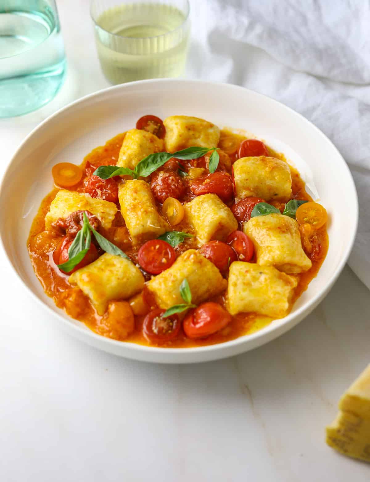 A close up of a white bowl filled with ricotta gnocchi, tomatoes and fresh basil