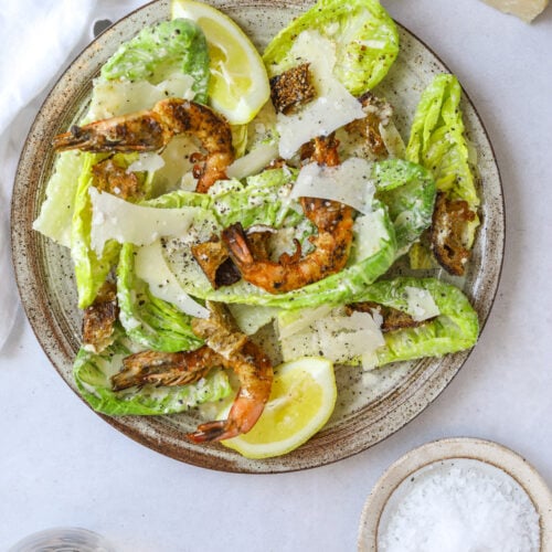 a plate with homemade caesar salad topped with grilled shrimp and shaved parmesan cheese