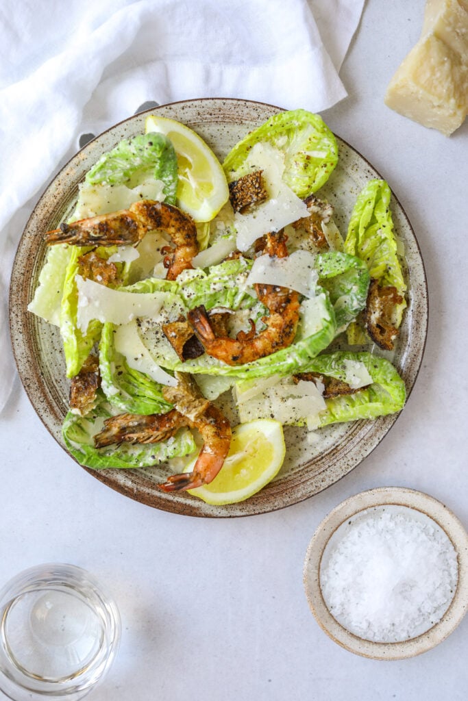 a plate with homemade caesar salad topped with grilled shrimp and shaved parmesan cheese