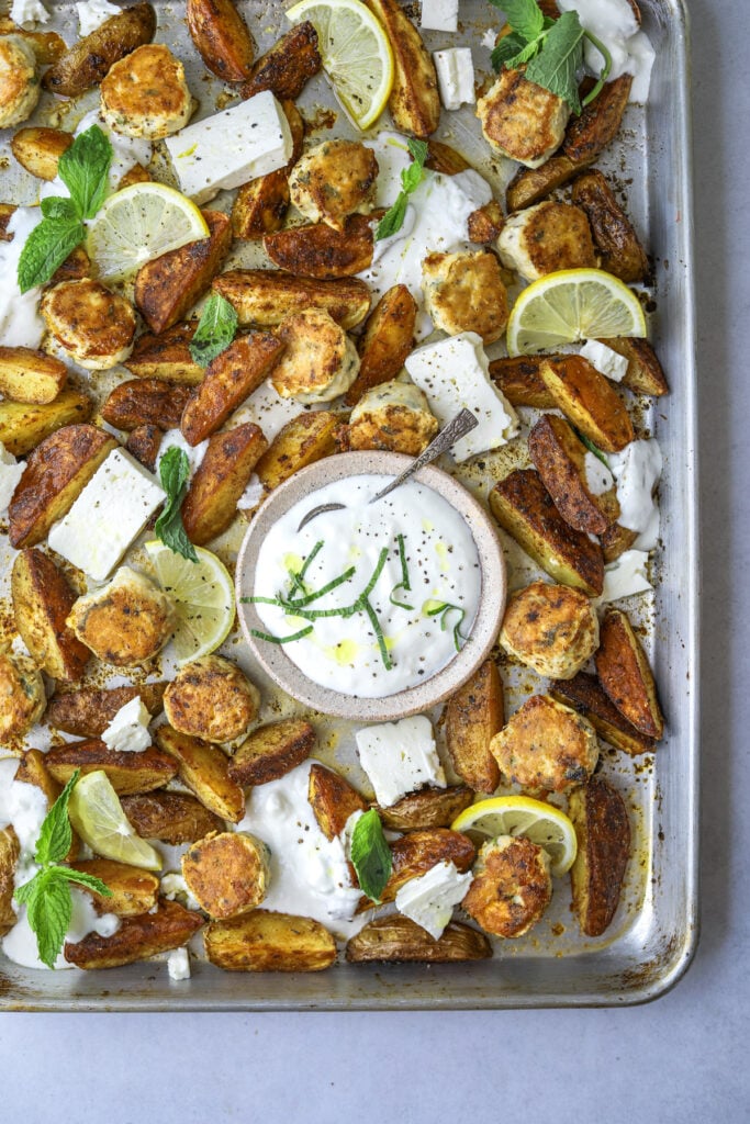 A sheet pan with chicken meat balls, potato wedges and a bowl of garlic feta yogurt
