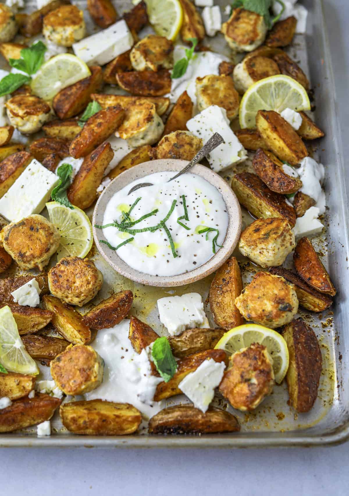 a sheet pan with greek chicken meatballs, potato wedges, feta cheese and fresh mint