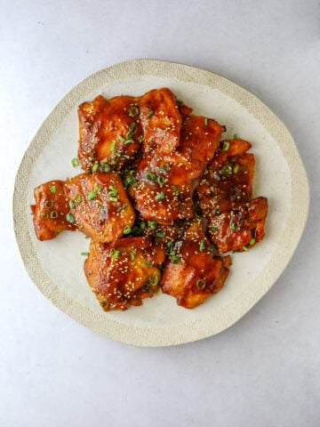 Sticky Chicken on a white plate topped with scallions and sesame seeds