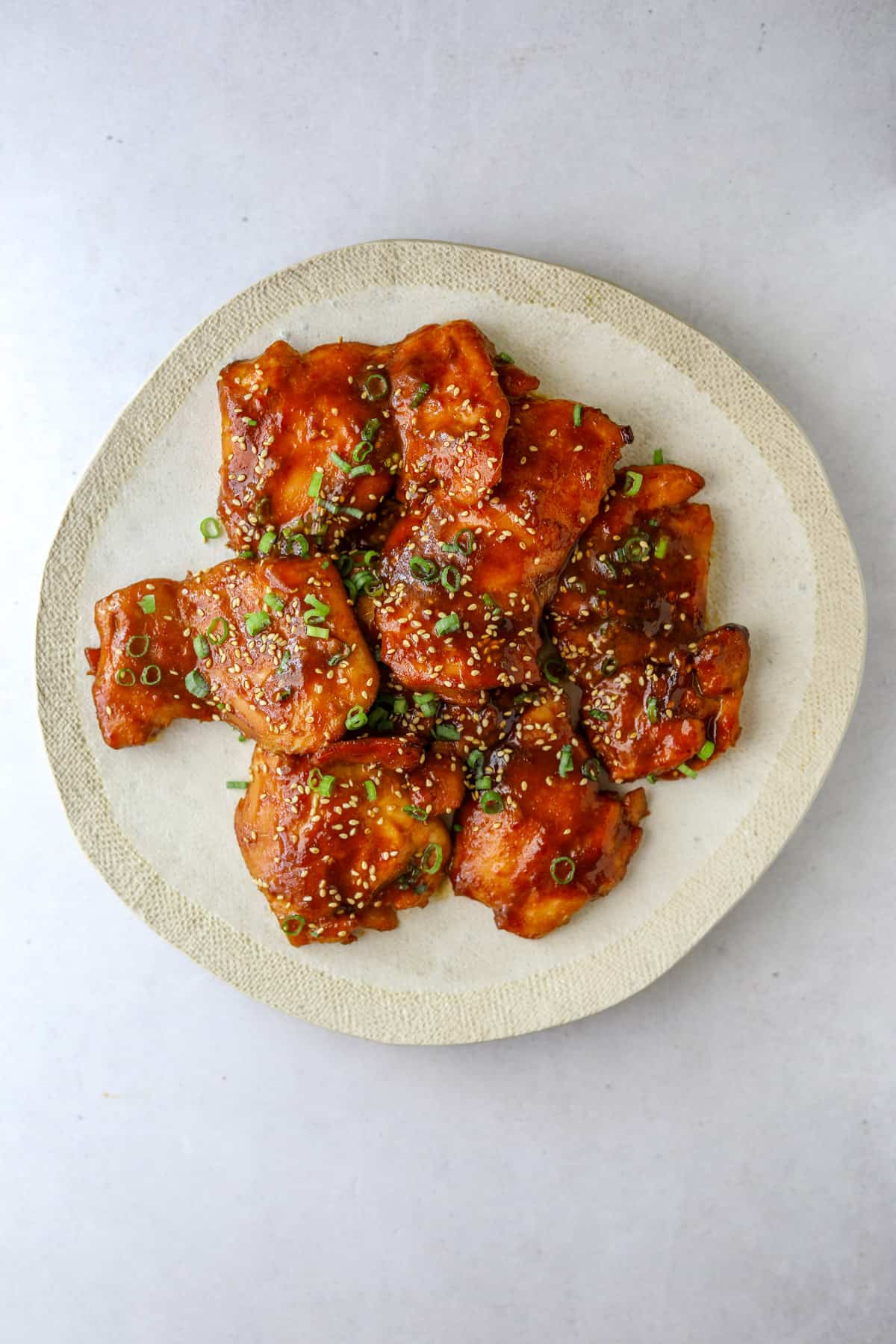 Sticky Chicken on a white plate topped with scallions and sesame seeds