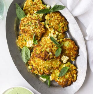 an oval tray filled with corn and zucchini fritters with basil
