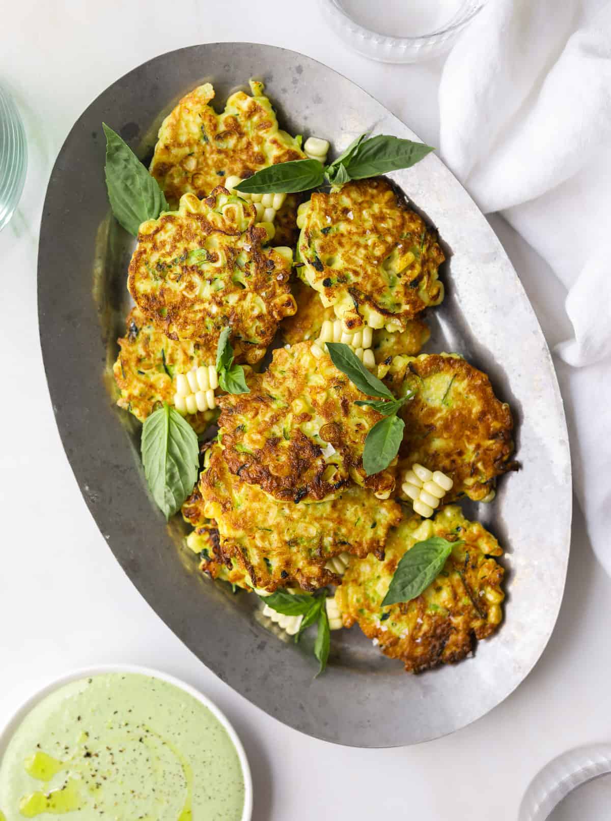 an oval tray filled with corn and zucchini fritters with basil