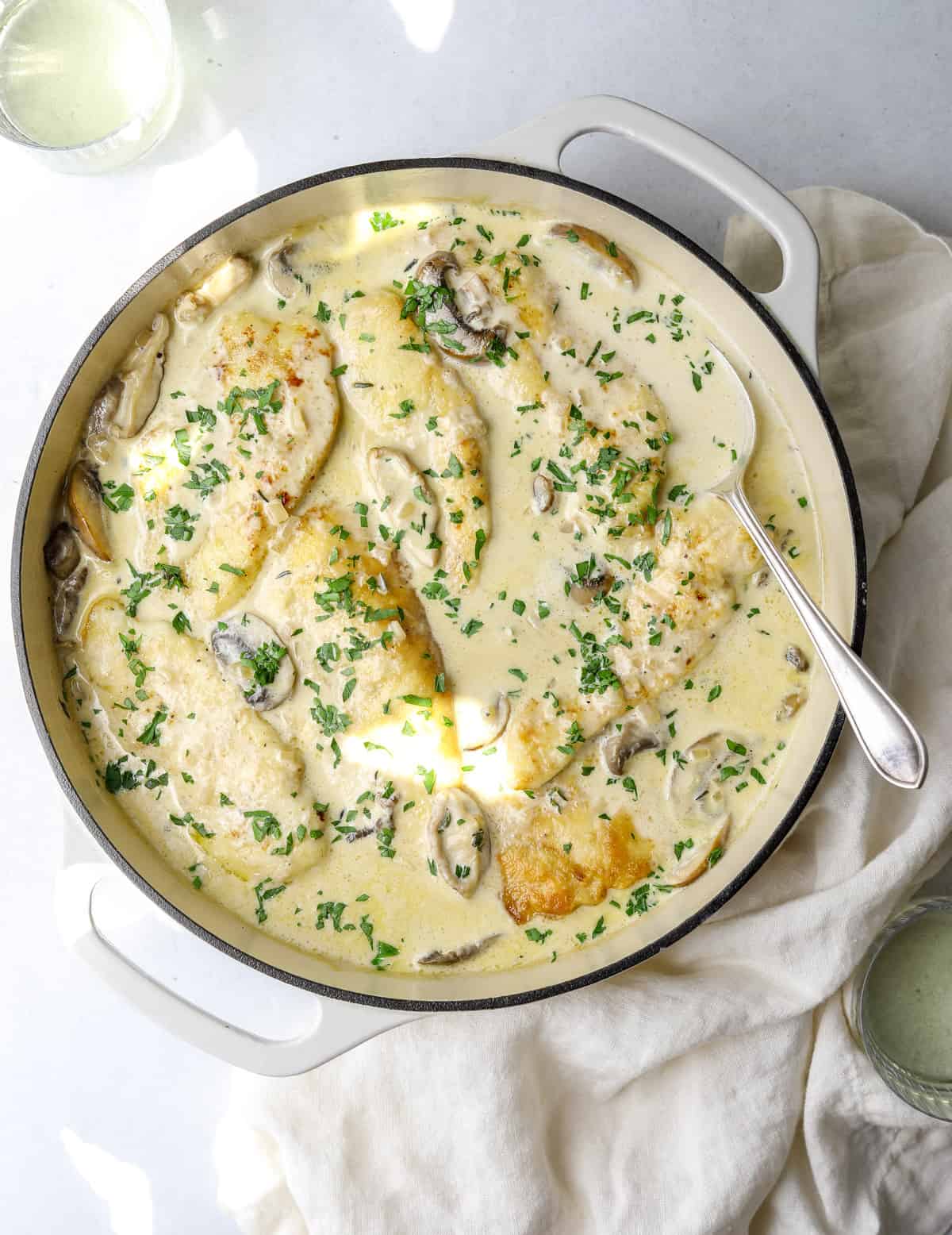 a pot filled with chicken in a mushroom cream sauce with a silver spoon and two glasses of wine