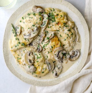 a white plate with chicken and mushroom sauce wand chopped parsley