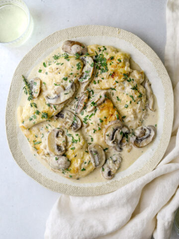 a white plate with chicken and mushroom sauce wand chopped parsley