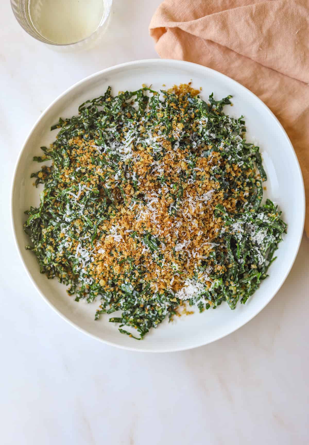 a white bowl filled with kale caesar salad with grated parmesan cheese