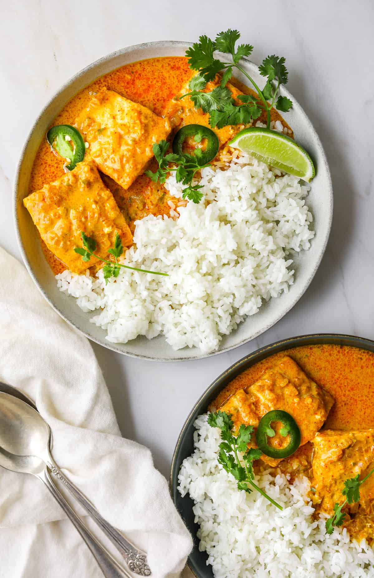 a white bowl filled with coconut curry braised salmon with limes, rice and cilantro