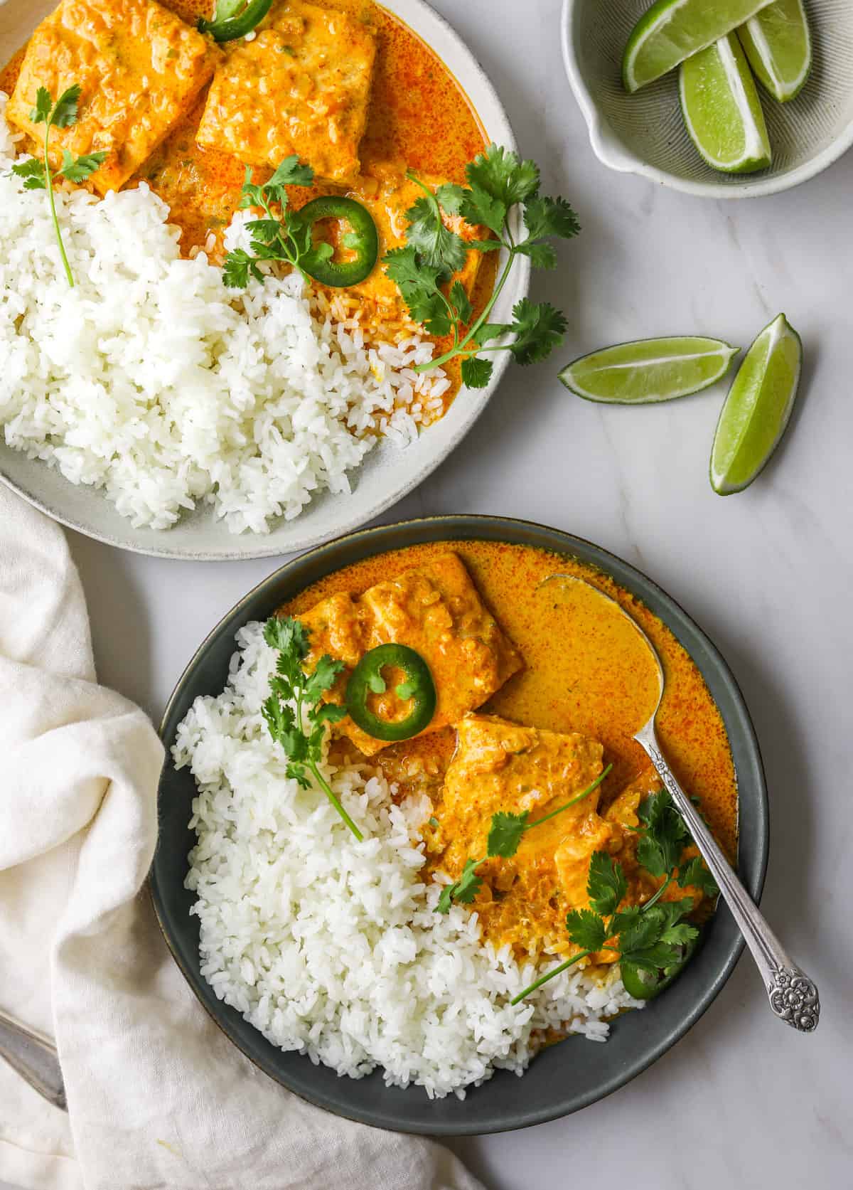 two bowls of coconut curry braised salmon with white rice, cilantro, jalapeños and lime wedges