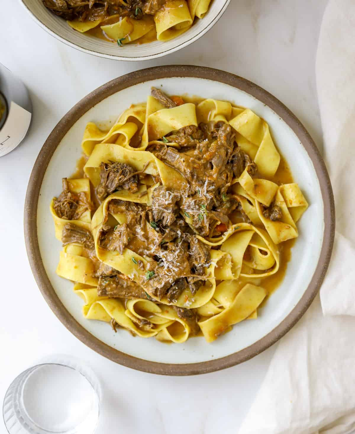 a plate of pappardelle pasta with braised short rib ragù with a bottle of wine and white linen napkin