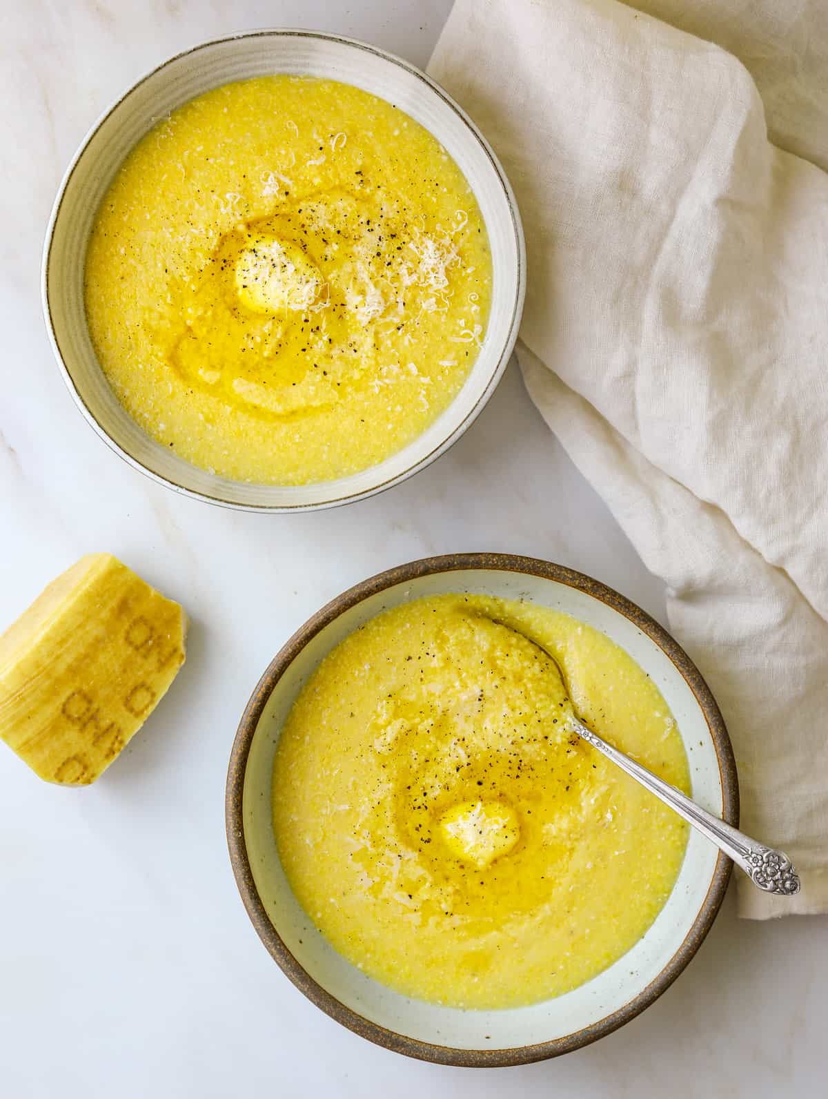 two bowls of polenta with a piece of parmesan cheese on the side