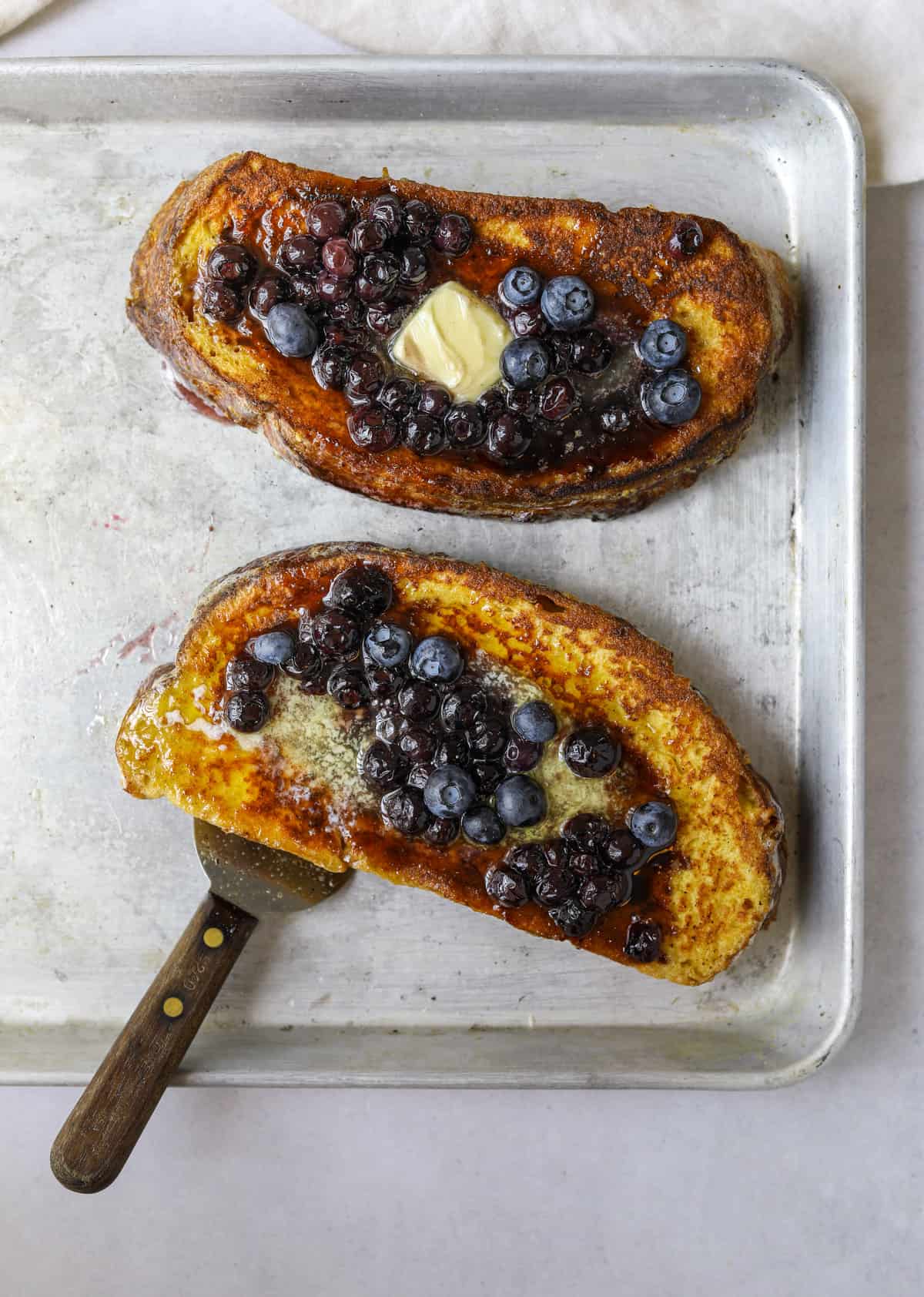 two slices of sourdough french toast on a baking tray with a spatula