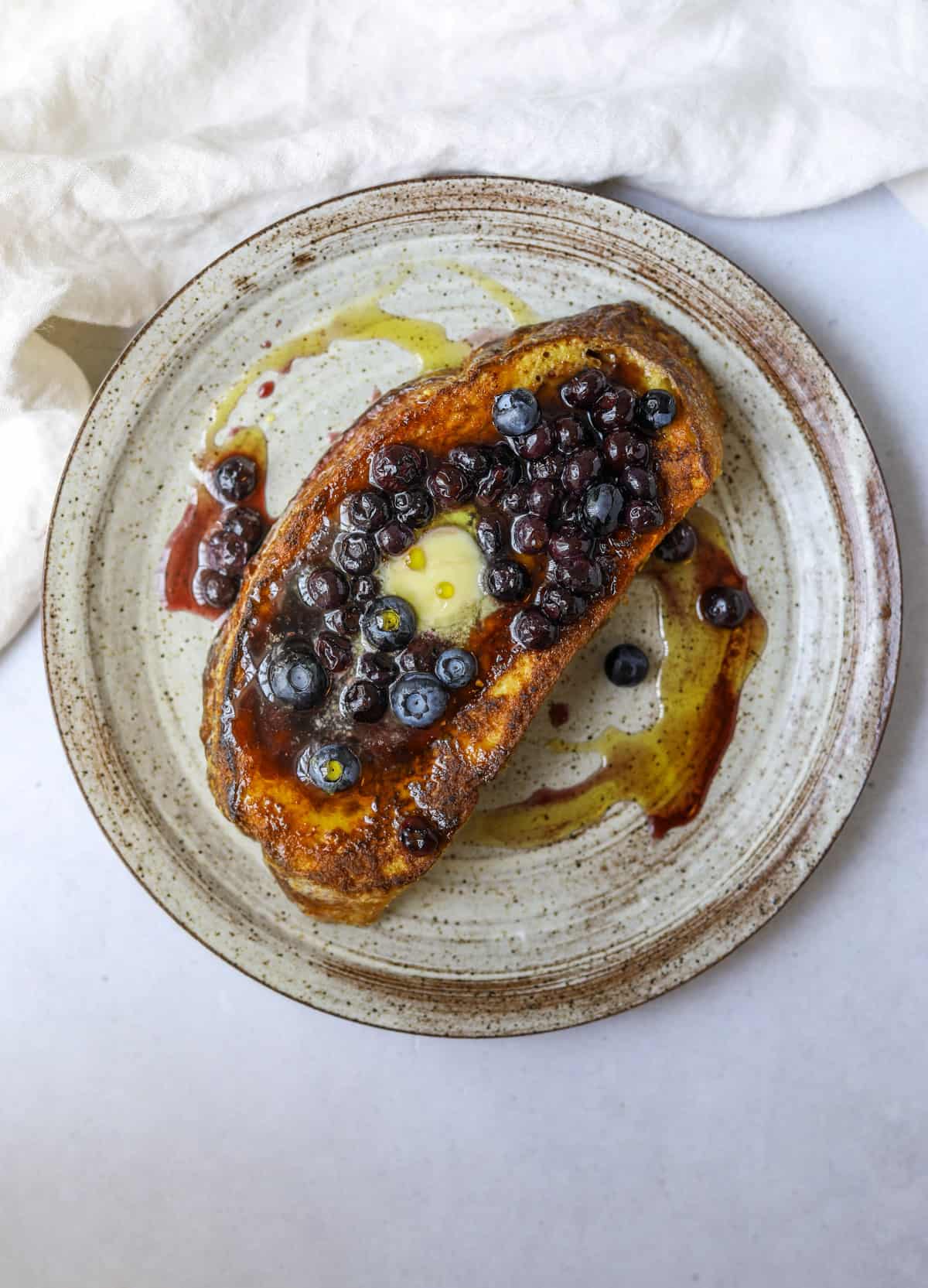a slice of sourdough french toast topped with blueberry sauce and butter