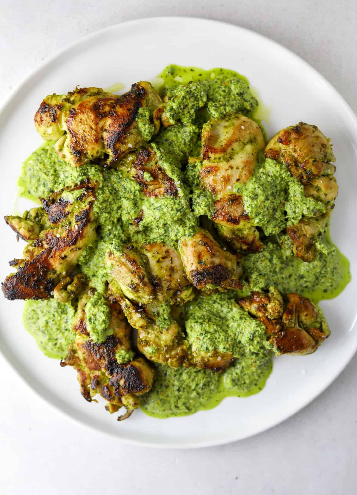 a white plate of chicken thighs with green sauce