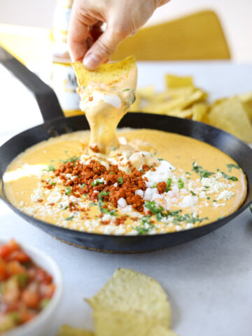 a tortilla chip dipping into a warm pot of melted queso and chorizo