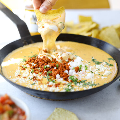a tortilla chip dipping into a warm pot of melted queso and chorizo