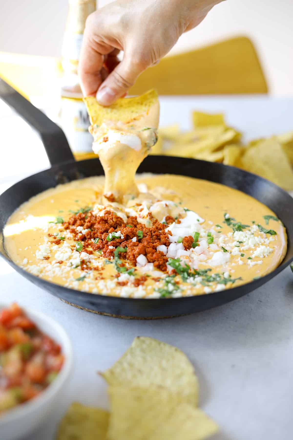 a tortilla chip dipping into a warm pot of melted queso and chorizo