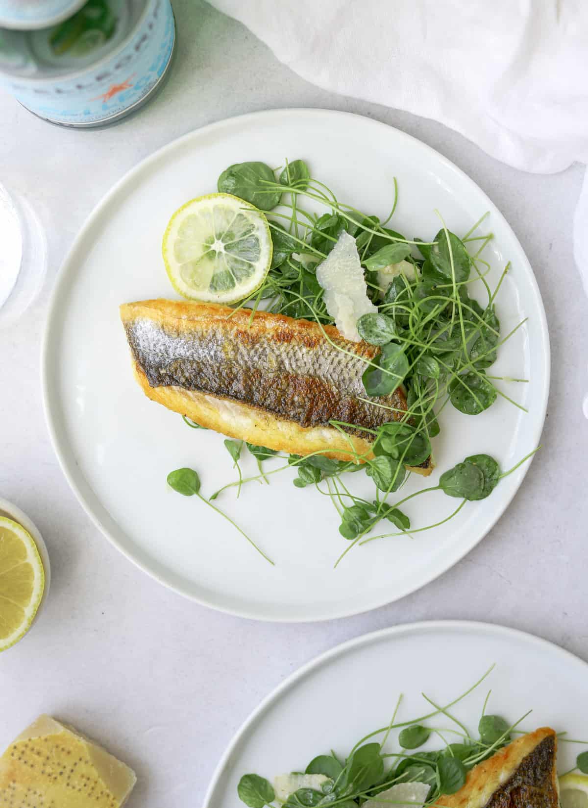 a white plate on a light blue background with branzino filets, watercress and lemon slices