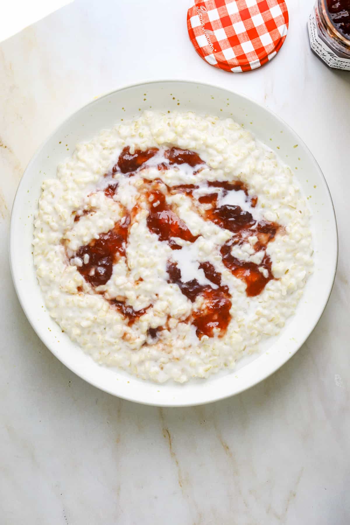 a white ceramic bowl of breakfast porridge with strawberry jam
