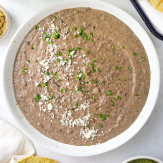 a bowl of puréed black beans topped with diced jalapeño and queso fresco