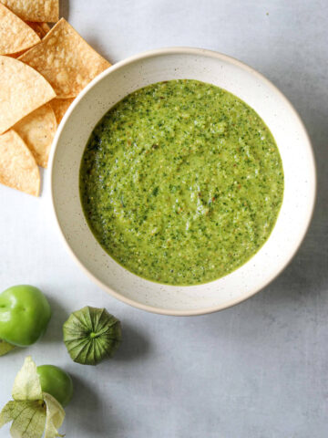 a white ceramic bowl filled with salsa verde and tortilla chips on the side