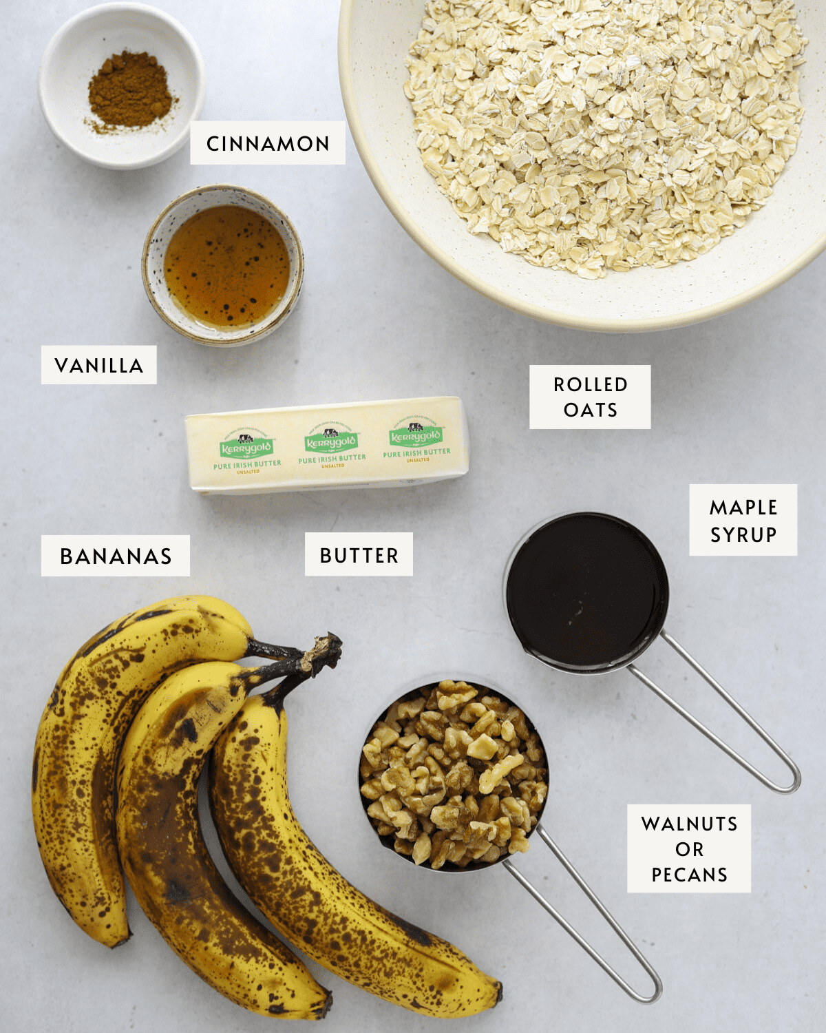 a bowl of rolled oats, three ripe bananas, maple syrup in a measuring cup, a stick of butter, chopped walnuts