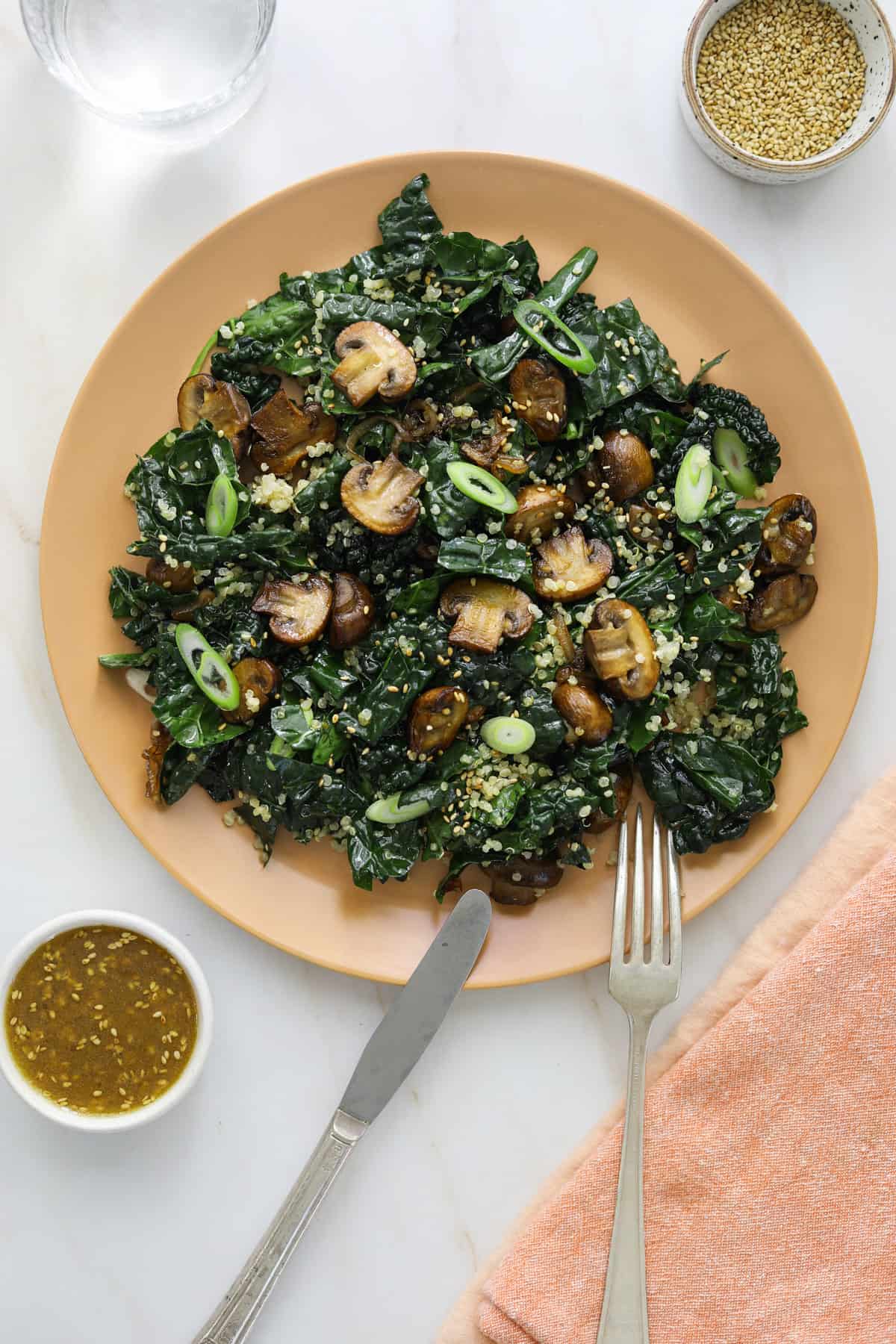 a pink plate on a blue background with kale, roasted mushrooms, sesame seeds and scallions