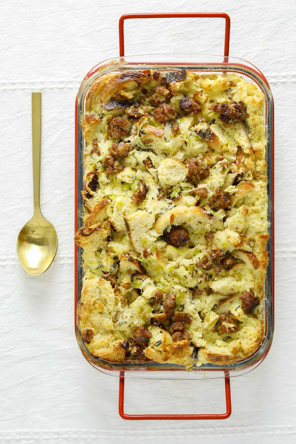 a rectangular glass baking dish with red handles filled with savory bread pudding with sausage.