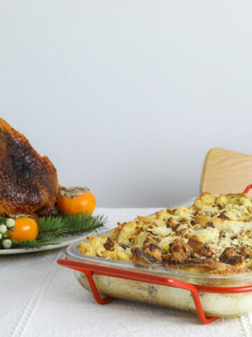 a table setting with a white table cloth, a whole roasted turkey, a glass off red wine and a baking dish with savory bread pudding