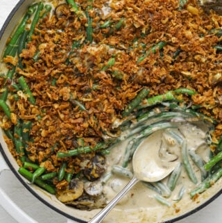 a close up of a white pan filled with green bean casserole with a silver spoon