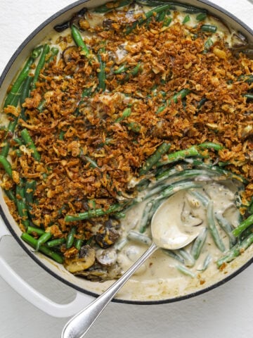 a close up of a white pan filled with green bean casserole with a silver spoon