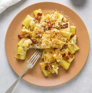 a pink plate with rigatoni carbonara with roasted cauliflower florets and bacon piece