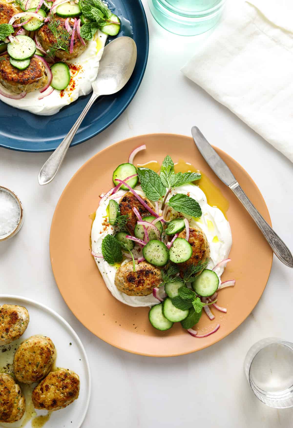 a peach colored plate with yogurt, meatballs and cucumber-herb salad.