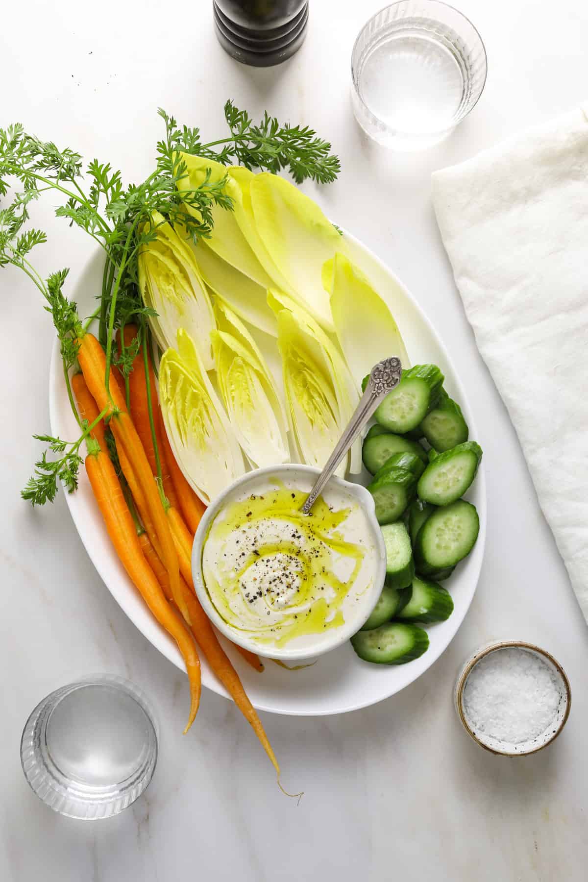 a white platter with carrots, cucumber, endive and small bowl of tahini labneh dip