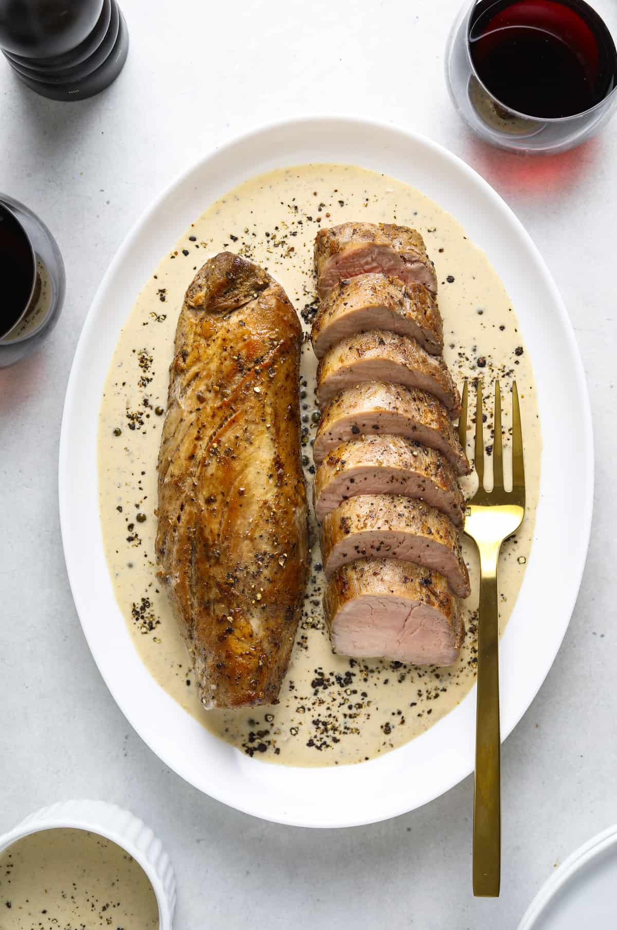 two roasted port tenderloins on a white platter with cream sauce