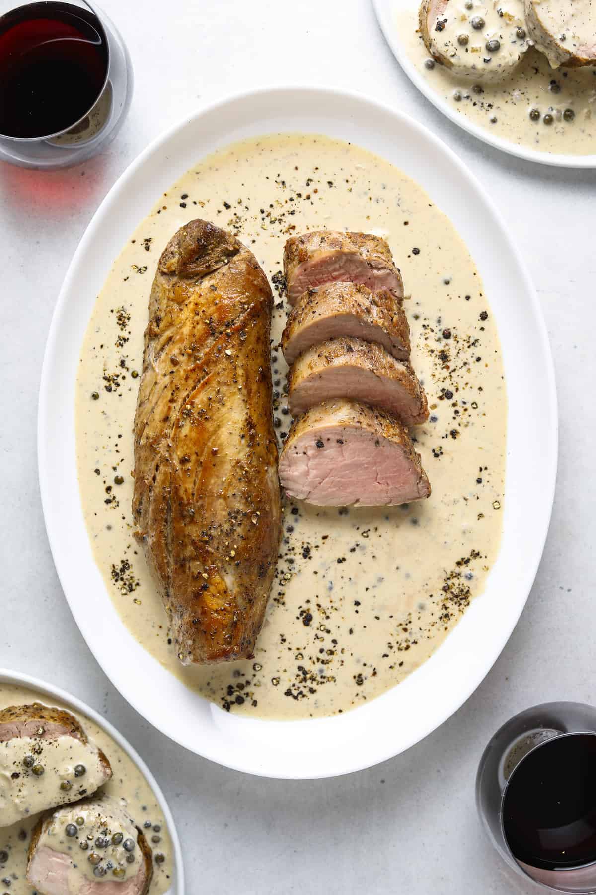 sliced pork tenderloin on an oval platter with cream sauce and lots of cracked black pepper