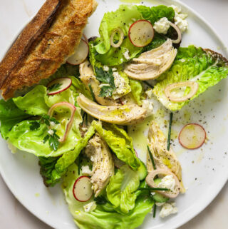a close up image of a salad on a white plate with torn baguette