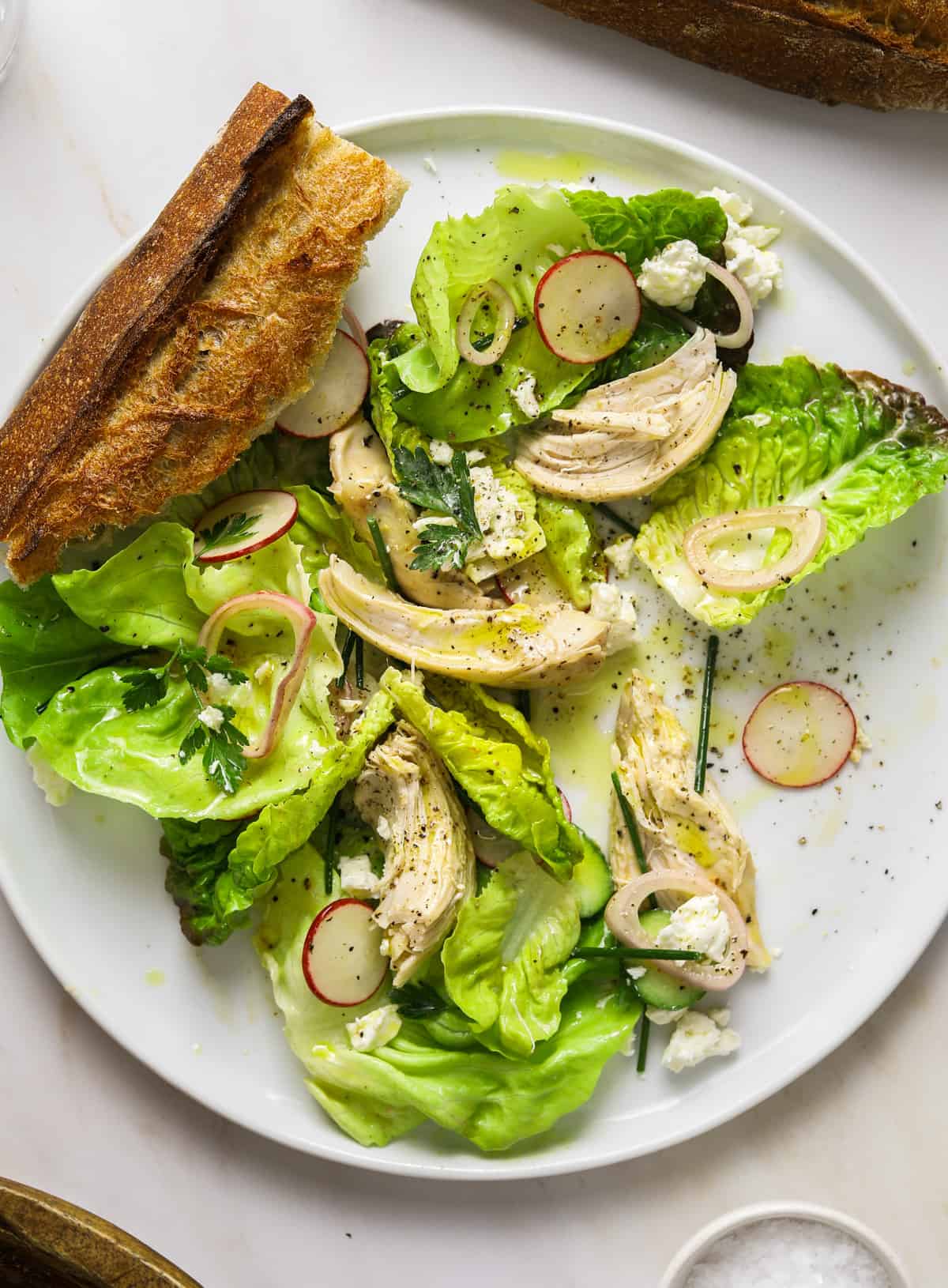 a close up image of a salad on a white plate with torn baguette