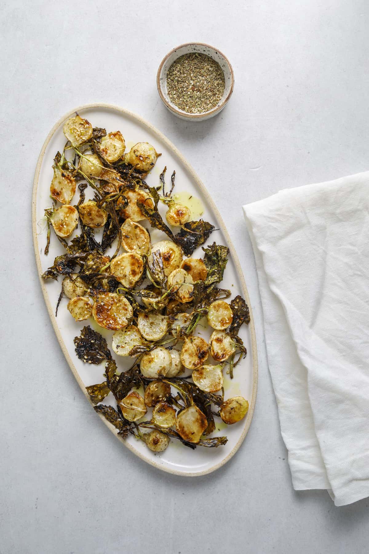 an oval platter with roasted baby turnips with a small dish of za'atar spice and a white linen napkin