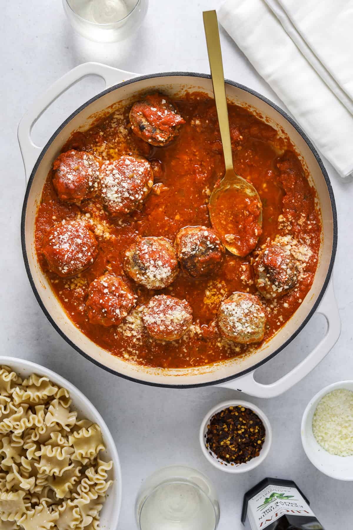 a dutch oven filled with meatballs and sauce with a gold spoon and a bowl of pasta on the side.