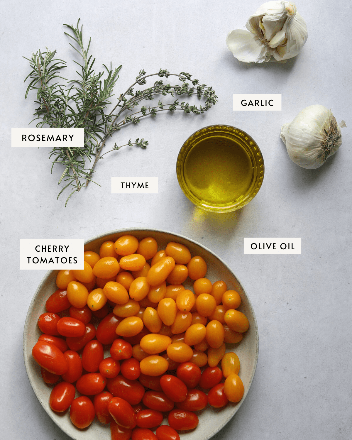 a bowl of yellow and red cherry tomatoes, fresh rosemary and thyme, garlic bulbs and olive oil