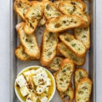 a baking tray with toasted crostini and a small dish of marinated feta cheese